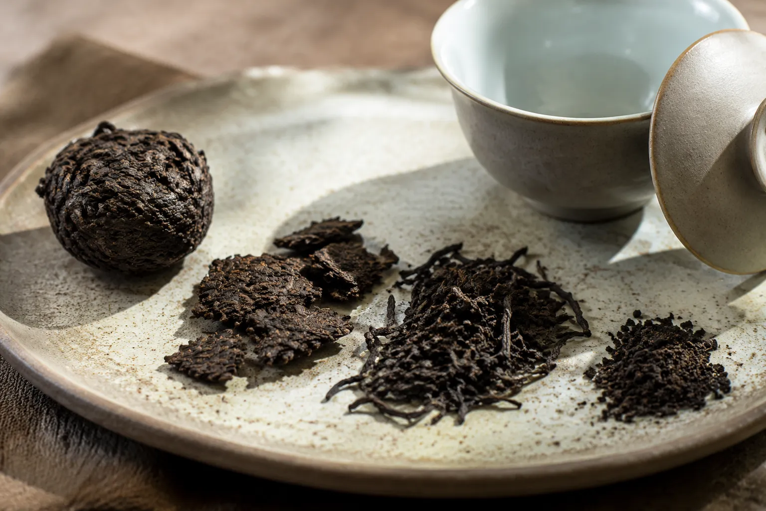 Compressed dark tea pieces, broken flakes, and crumbs separated near a gaiwan for gongfu brewing