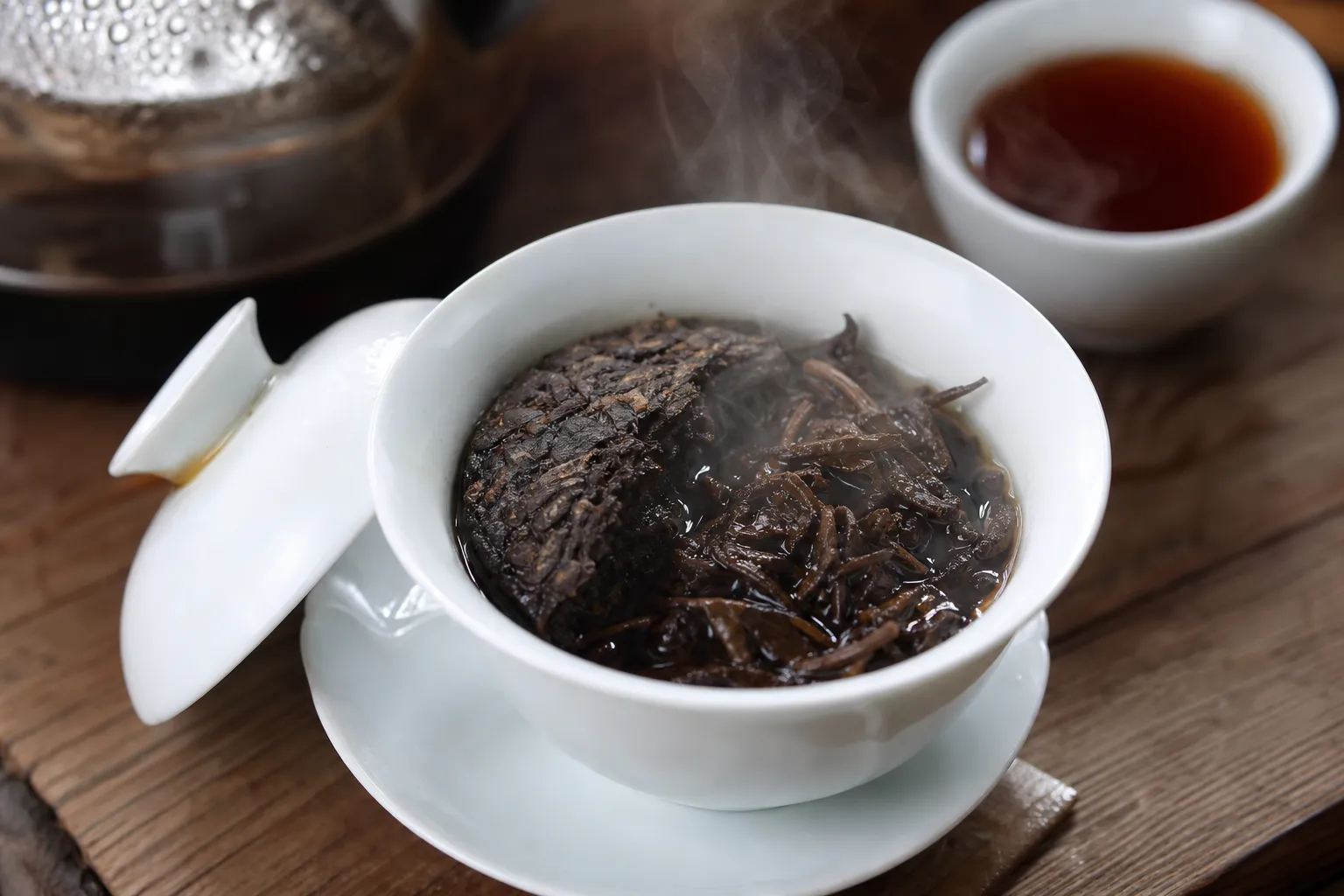 A compact piece of dark tea loosening beside a gaiwan during a short hot infusion
