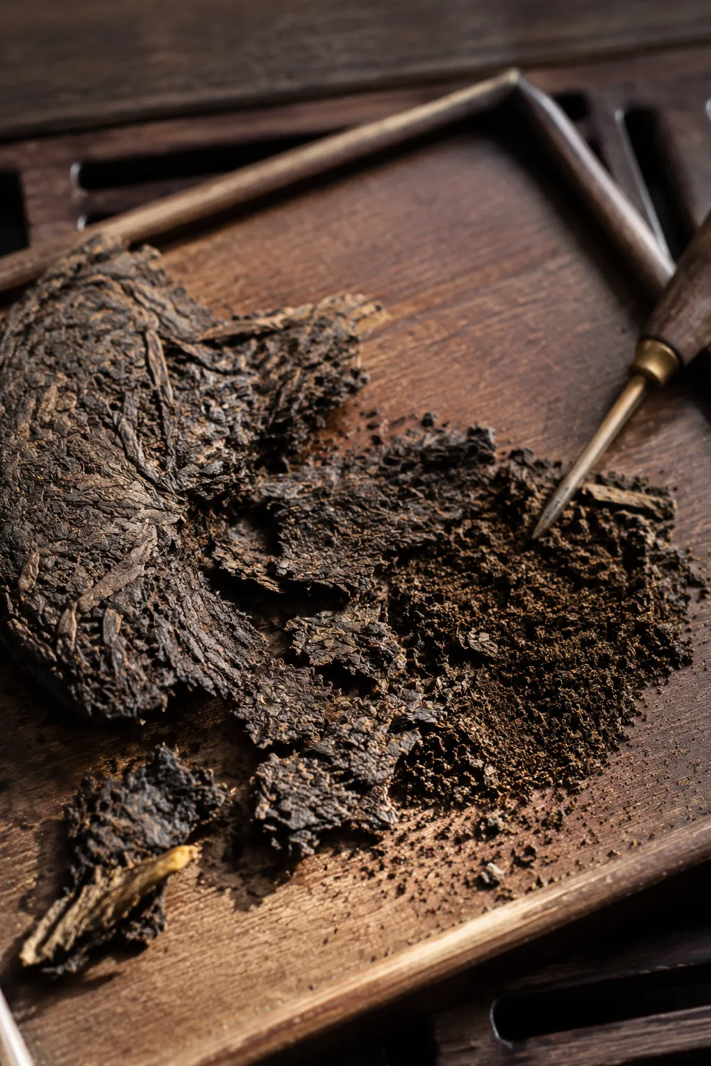 Compressed dark tea opened into larger flakes beside a small pile of fine crumbs and dust for judging tool pressure.