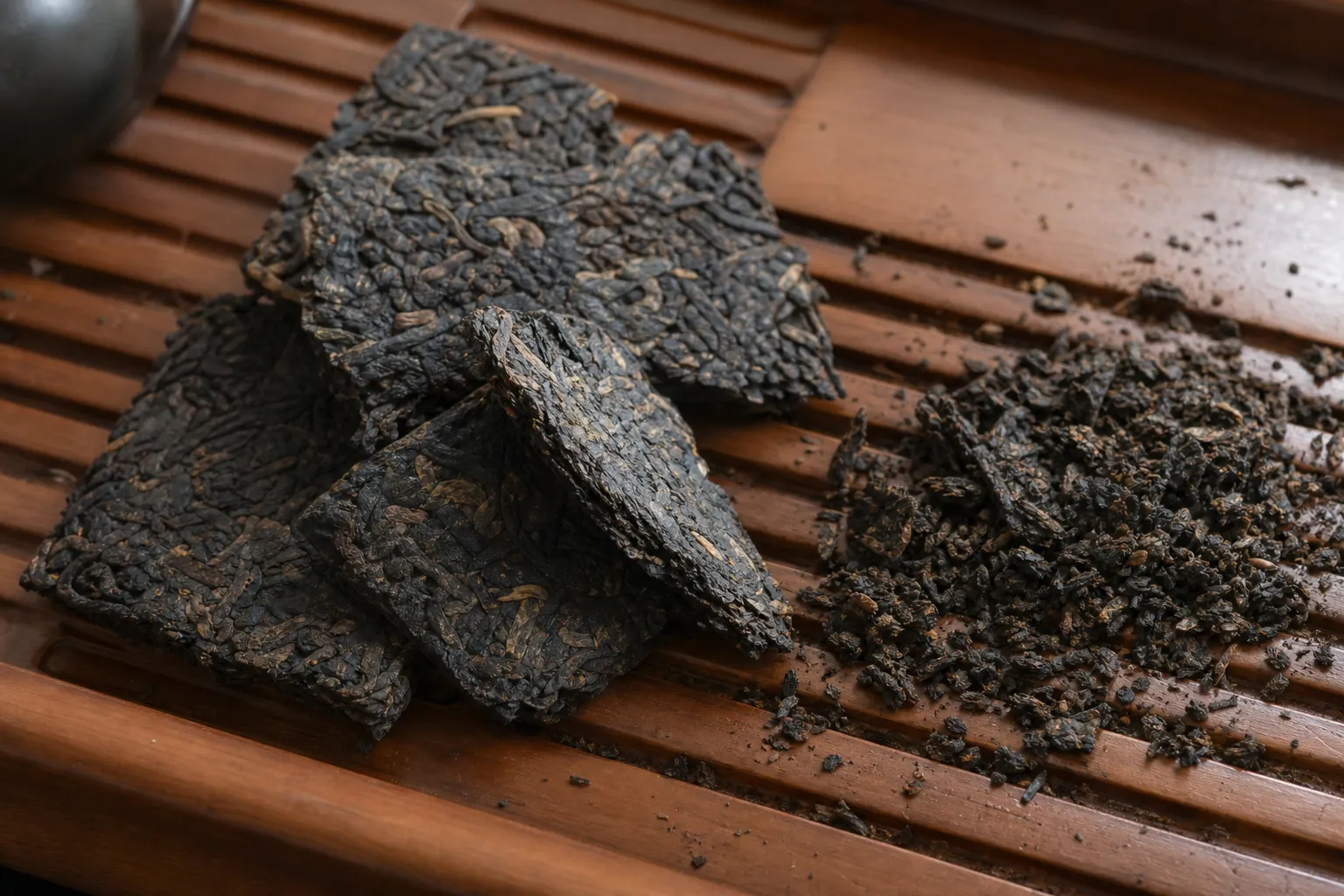 Small dark tea brick fragments showing intact flakes, crumbs, and a controlled break area after loosening